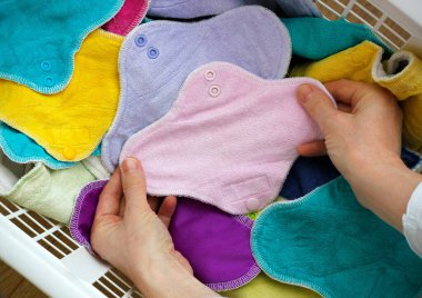 Çamaşır sepetinin içinde pembe bir bez pedi tutan kadın elleri renkli bambu yıkanabilir peçetelerle dolu. Çevre dostu yeniden kullanılabilir kumaş pedleri, sıfır atık alternatif. Kadın hijyen kavramı