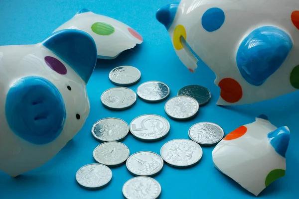 Broken ceramic dotted children\'s piggy bank with Czech crown coins on light blue background. Close up of smashed piggy bank and coins. Saving money by children and financial literacy concept.