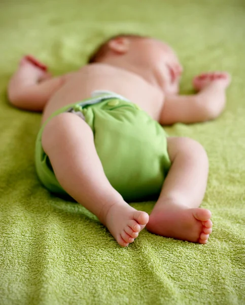 stock image Close up of cute bare feet of 1-month old baby wearing green cloth diaper and sleeping on green towel in bed. Eco friendly reusable baby diaper. Sustainable life, zero waste concept.