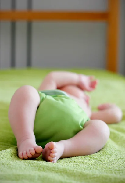 Close up of cute bare feet of 1-month old baby wearing green cloth diaper and sleeping on green towel in bed. Eco friendly reusable baby diaper. Sustainable life, zero waste concept.