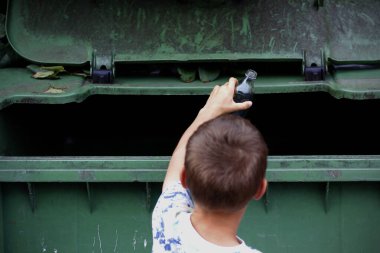 Beyaz bir çocuğun yeşil bir geri dönüşüm konteynırına boş cam şişe attığını gördüm. Çöpü farklı konteynırlara ayırmak. Çöp geri dönüşümü konsepti. Günlük işler yapan çocuk konsepti