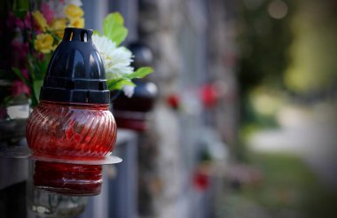 Kolumbaryum duvarındaki bir mezara bir mum ve yapay çiçek süslemesi yakın. Ölen akrabalarımızın anısına bir sembol. Ruhlar Günü konsepti. Azizler Günü
