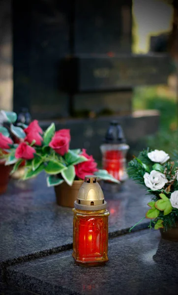 Close up of a burning candle and flower decoration on the grave. Symbol of remembrance of our deceased relatives. All Souls\' Day concept. All Saints Day