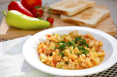 Kırmızı biber, domates, soğan, yumurta ve soya peyniri içeren sebze yemeği beyaz tabakta servis ediliyor. Lezzetli leço ve içindekiler bahçe masasında..