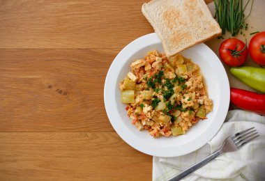 Kırmızı biber, domates, soğan, yumurta ve soya peyniri içeren sebze yemeği beyaz tabakta servis ediliyor. Lezzetli leço ve içindekiler ahşap masada fotokopi alanı ile.