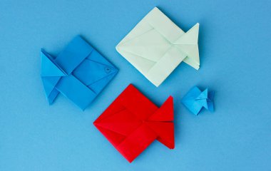 Üç büyük renkli origami kağıt balığı ve bir küçük balık mavi arka planda bir çocuk tarafından yapılmış. Renkli arka planda renkli origami balıklarının üst görünümü. Çocuk kağıt işi..