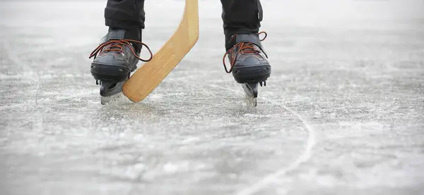 Ice skates and a hockey stick close-up. Legs of a boy playing ice hockey on a frozen pond or in ice rink. Winter activities concept.