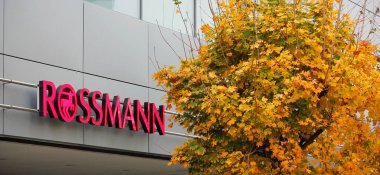 Prag, Çek Cumhuriyeti - 4 Kasım 2024: Atari salonunun girişinde şirket imzası ve şirketin adı Rossmann, yanında sarı sonbahar yaprakları olan akçaağaç taç.
