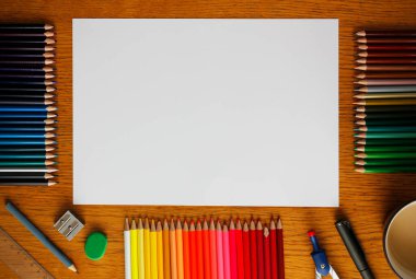 Tahta bir masanın üzerinde boş beyaz bir kağıt, pastel boyalar, diğer çizim malzemeleri ve yakınlardaki bir fincan kahve. Fotokopi alanı olan düz çizim. Taklit çiziliyor.