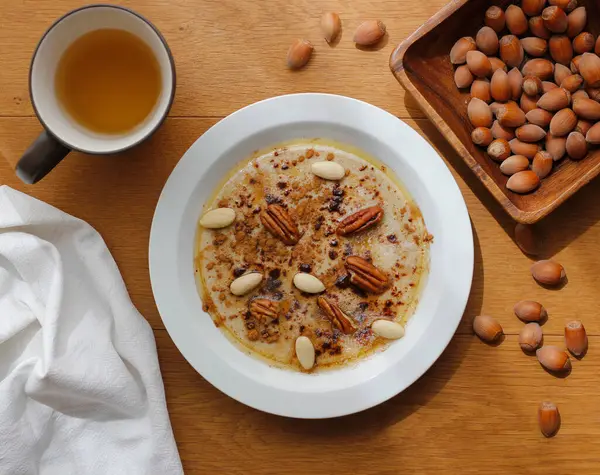 Karabuğday ve mısır irmiğinden pişirilmiş sağlıklı glütensiz yulaf lapası ve beyaz tabakta tarçın, akçaağaç şurubu, tereyağı ve fındık ile servis ediliyor. Sabah yulaf lapası ve fındık fincanıyla yatıyordu.