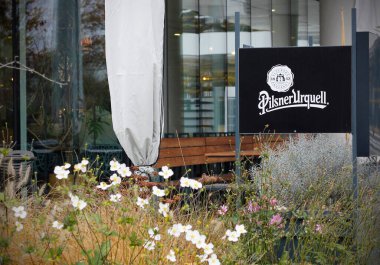 Prag 'da modern bir restoranın önündeki Pilsner Urquell bira tabelası, sonbahar çiçekleri ve ahşap bankların olduğu açık hava oturma alanı. Popüler bir Çek bira markasının editör görüntüsü