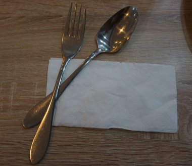 Fork with spoon and tissue paper on a wooden table in a cafe.