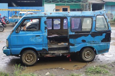 Indonesian public transportation, old and damaged blue angkot, parked on the side of the main road