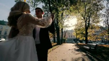Yeni evliler sonbahar parkında dans ediyorlar. Damat gelini kollarına alır.
