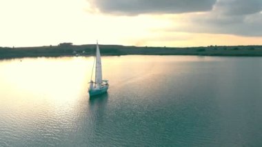 Gün batımında açık denizde hava manzaralı bir yat. Gün batımında yatın yanında yelkenli manzaralı bir uçuş. Güneş suya yansıyor.