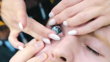 Kontakt lensler mavi gözlü bir erkeğin gözüne takılır. Bir kadının parmaklarına yakın plan kontak lens takması.