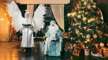 Noel 'de Noel ağacı ve hediyelerin yanında Aziz Nicholas ve Melek. Yeni Yıl Selamları