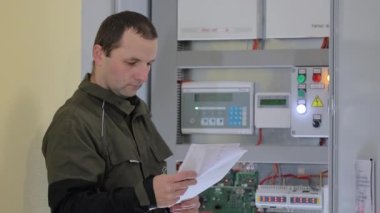 Bir elektrikçi elektrik santralini kontrol ediyor. Mühendis talimatları ve diyagramı okur ve elektrik şebekesinin işleyişini teşhis eder.