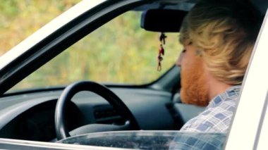 A drunk man with a yellow beard sits in an old car.