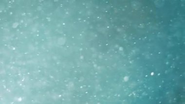 Blurred background of turquoise color and many particles blurred in the air. Imitation of snow on a turquoise background.