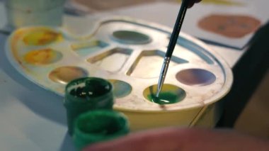 A child. The artist dilutes green paint with water, close-up.