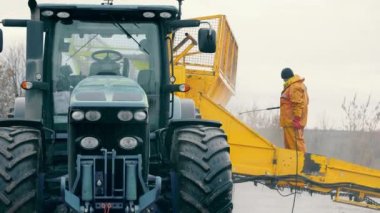 Washing of large-sized agricultural machinery. A worker in a yellow suit washes a tractor trailer