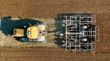 Aerial top view A tractor plows a field with a harrow system. Preparation of agricultural land for spring sowing