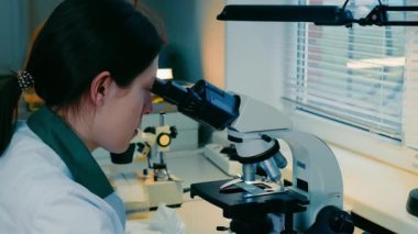 Dişi mikrobiyolog mikroskop altında bakteri arıyor. Bir araştırmacı, mikroskop kullanarak topraktaki çeşitli bakterileri inceler.