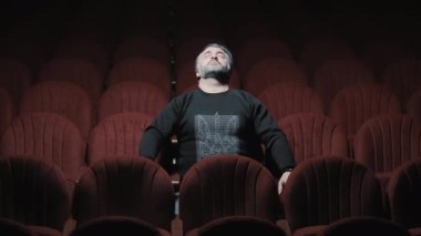 Opera salonunun büyük salonunda, gözleri kapalı bir sandalyede tek başına oturan bir adam. Kırmızı sandalyeli, karanlık bir salonda rüya gibi, yalnız bir adam.