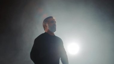 Sahnede şarkı söyleyen bir opera sanatçısının silueti arka planda ve hafif bir dumandır.