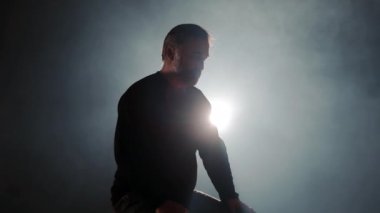 Işık ve dumanla aydınlatılmış bir sandalyede tek başına oturan yaşlı bir adamın silüeti. Karanlık bir odada yalnız bir adam