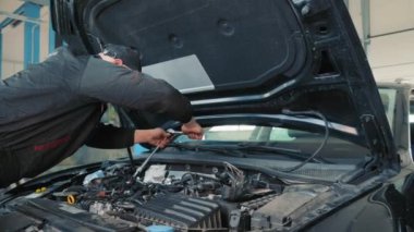 Bir araba tamircisi yolcu arabasının motorunu tamir eder. Çalışan fındıkları özel bir anahtarla sıkıyor.