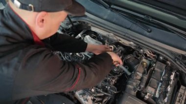 Bir araba tamircisi yolcu arabasının motorunu tamir eder. Çalışan fındıkları özel bir anahtarla sıkıyor.