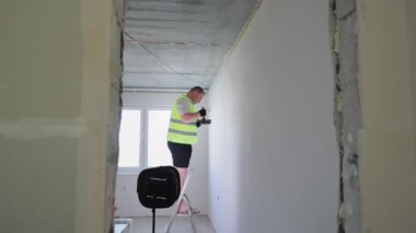 Restorasyon odada işe yarıyor. Zanaatkar bir merdiven üzerinde durur ve bir fırçayla duvarı beyaza boyar.