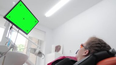 Modern dişçilik. Kromakey. Hasta dişçi koltuğunda yatıyor ve yeşil ekrana bakıyor.