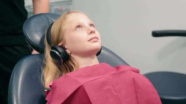 Κορίτσι Κάθεται Στην Οδοντιατρική Καρέκλα Και Ακούει Μουσική Σύγχρονη Παιδιατρική — Αρχείο Βίντεο