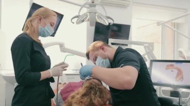 Bir diş hekimi ve koruyucu maskeli asistanı bir diş kliniğinde hastaların dişlerini tedavi eder. Sağlık ve tıp konsepti. Modern diş sağlığı kliniği.