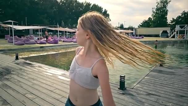 スローモーションで濡れた髪のダンスを持つ小さなブロンドの少女 少女は自分の周りを回っている 自由な子供が湖やビーチの背景で屋外で踊っています — ストック動画