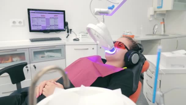 在Led美白过程中戴防护眼镜的病人坐在诊所的椅子上 现代牙科诊所的牙齿光洁化 — 图库视频影像