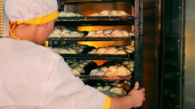 Dişi fırıncı fırından yeni çıkmış örülmüş ekmek ile taşınabilir rafı alıyor. Beyaz üniformalı bir kadın ve Cap dükkâna pasta götürüyor..