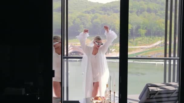一个戴着白色太阳镜 白色睡衣和白色丝绸长袍的快乐新娘在阳台上跳舞 快乐新娘的早晨 — 图库视频影像