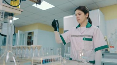 Odaklanmış Bilim Adamı mavi kimyasal sıvıyla Test Tüpü 'nü inceliyor. Laboratuvar üniformalı ve eldivenli koyu renk saçlı kadın laboratuvar analizi yapıyor. Biyokimya Konsepti.