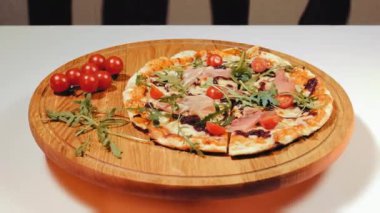 İştah açıcı pizza dönüşümlü ve kirazlı domateslerle ahşap bir tahtanın üzerinde yatıyor. Prosciutto, roka ve domatesli fırında pizza. Lezzetli fast food. Kapat..