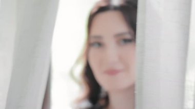 Beyaz perdenin arkasında saklanan gelinlerin yüzlerini yakından çek. Mutlu kadın perdenin arkasından kameraya bakıyor..