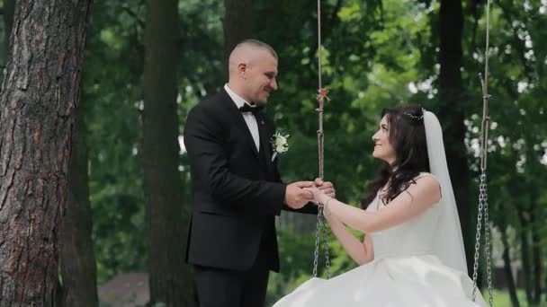 花嫁はスイングの上に座っており 花嫁は女性の手を握っています 春の日 結婚式 カップル 公園で過ごす時間を過ごす — ストック動画