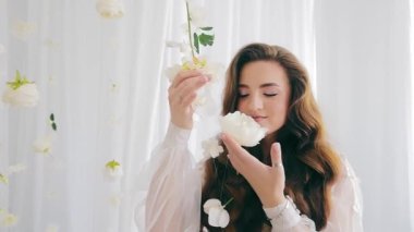 Mutlu bir gelin beyaz bir çiçeği kokluyor. Güzel bir salonda beyaz bir elbise içinde güzel bir gelin..