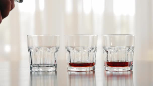 一个人的手把酒倒进杯子里 靠近点三杯含酒精的威士忌加在其中一杯中 — 图库视频影像