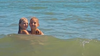 İki kız çocuk denizde yüzüyor ve kameraya poz veriyor, sarılıyorlar. Mutlu bir çocukluk. İki kız kardeş, denizde dinleniyorlar, yüzüyorlar.