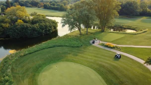 有两辆高尔夫球车在高尔夫球场上行驶 美丽的风景 树木和湖泊 俯瞰美丽的高尔夫球场 靠近湖畔 还有两辆高尔夫球车 国家俱乐部假期 — 图库视频影像