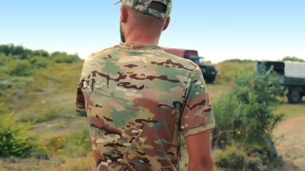 軍人が現場を歩き回り カモフラージュのTシャツとキャップを着て 前景を眺めている 戦争と平和という概念 — ストック動画